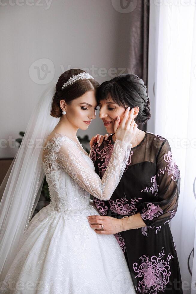 A beautiful and happy mother and her daughter, the bride, are standing next to each other. The best day for parents. Tender moments at the wedding. photo
