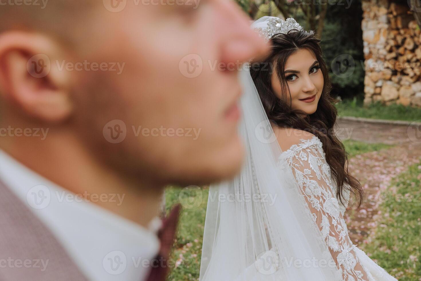 A handsome groom in the spring forest stands in front of his bride. Beautiful wedding white dress. Walks in the park. A happy and loving couple. photo