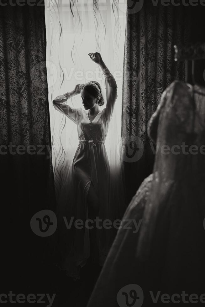 a woman standing in front of a window in a dressing gown on a wedding morning. Black and white photo. photo