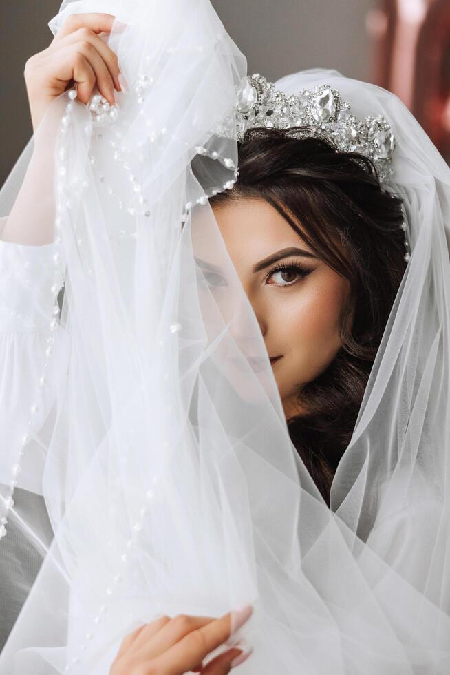 A beautiful brunette bride with a tiara in her hair is getting ready for the wedding in a beautiful robe in boudoir style. Close-up wedding portrait, photo. photo