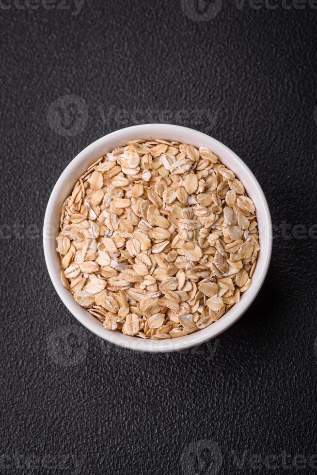 Raw oatmeal flakes in a ceramic bowl on a dark concrete background photo