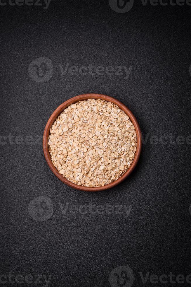 Raw oatmeal flakes in a ceramic bowl on a dark concrete background photo