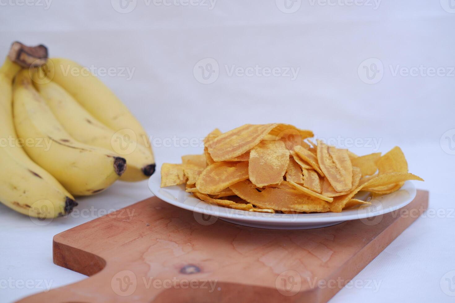 Crispy banana chips on a white plate with fresh bananas. photo