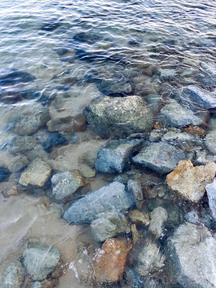 el superficie de el mar es un vibrante lona de resumen patrones, como olas descanso en contra el rocoso costa, formando un asombroso fondo de pantalla de de la naturaleza arte. foto