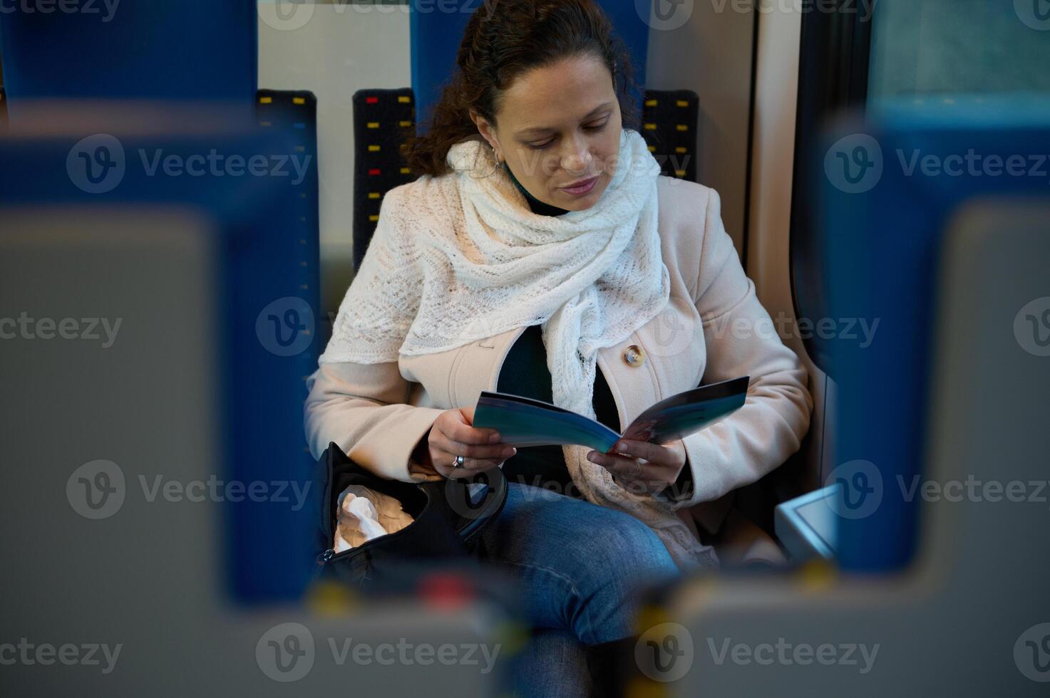 Confident young businesswoman 40 years old, enjoying her business trip, reading leaflet while commuting to work on high-speed comfortable train. People. Business. Railroad transportation. Lifestyle photo