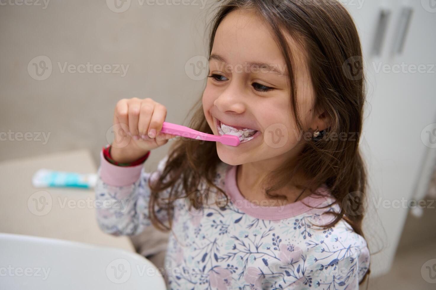 Adorable little child girl brushing teeth in front of the mirror in the home bathroom photo