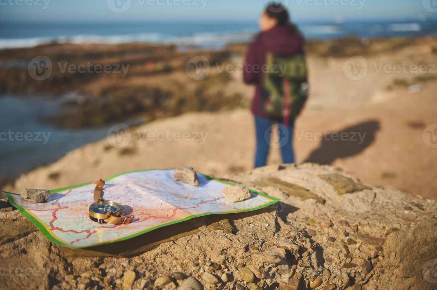 Selective focus on compass and map on the rock over blurred background of a backpack female tourist enjoying his journey photo