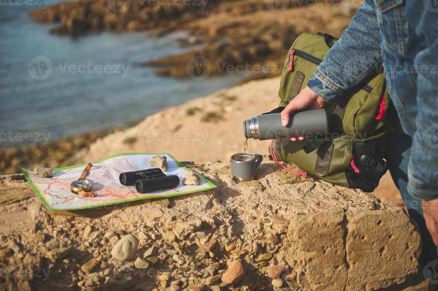 Close-up of a tourist hand holding thermos flask and pouring hot tea drink into a stainless steel mag photo