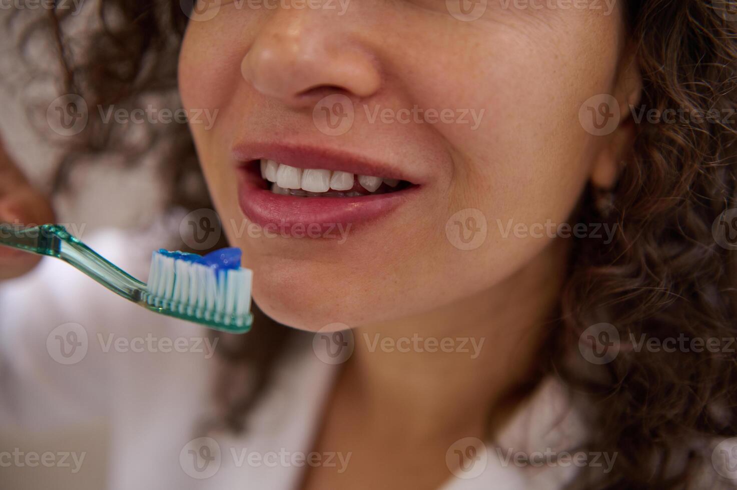 Cropped shot of a young beautiful woman holding toothbrush near her mouth, brushing white healthy teeth in the bathroom. photo