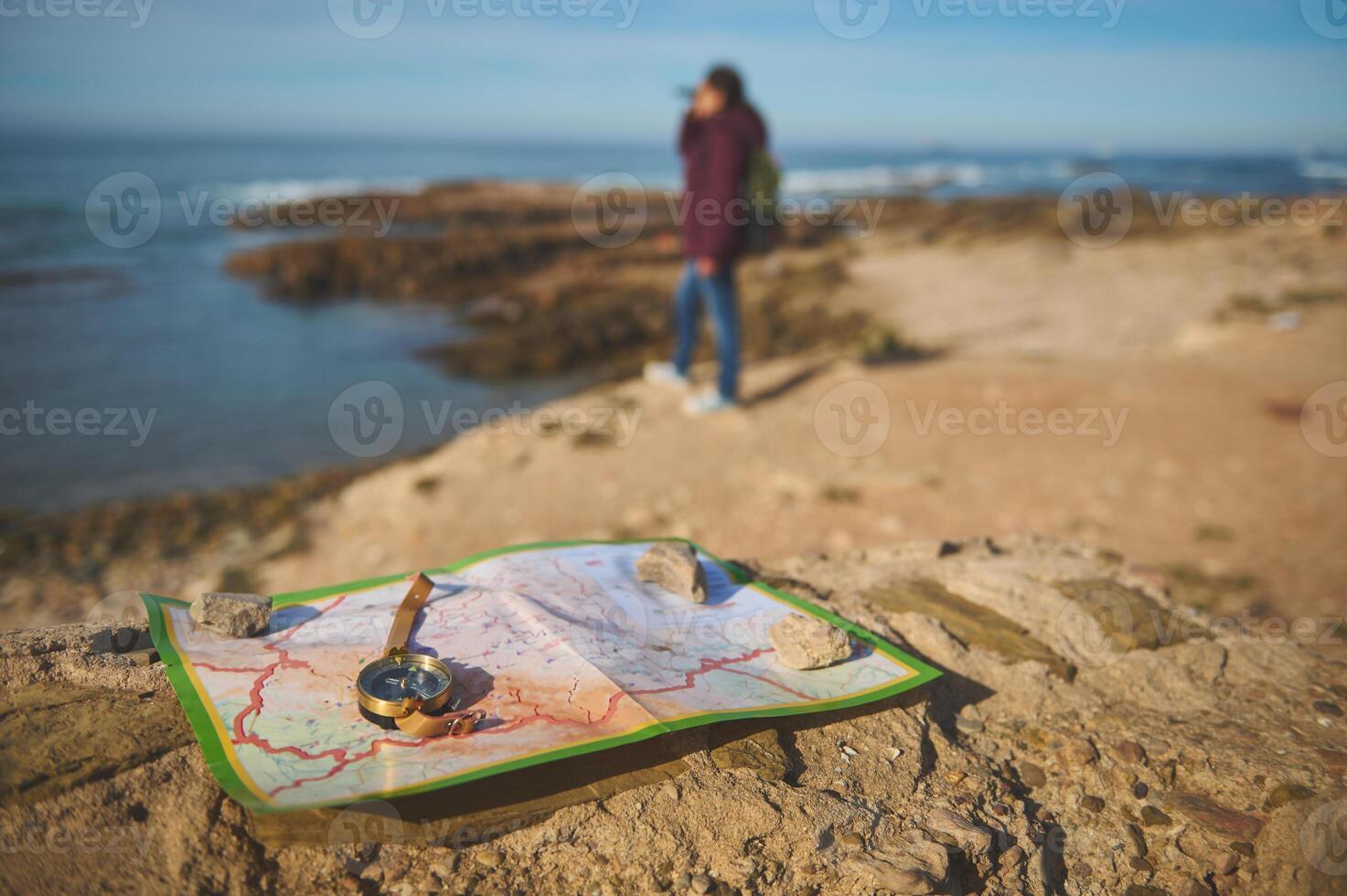 Details on a compass and map on a rock against blurred female tourist looking into the distance through binoculars photo