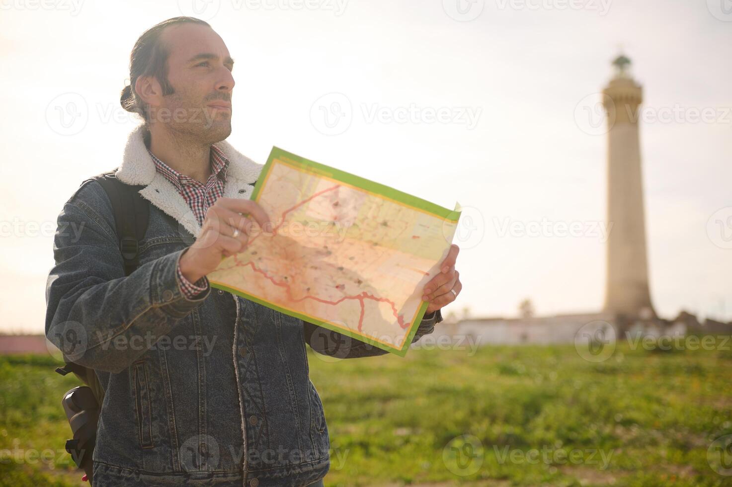 Caucasian mid adult man standing with a map against the background of a lighthouse, exploring the nature and city photo