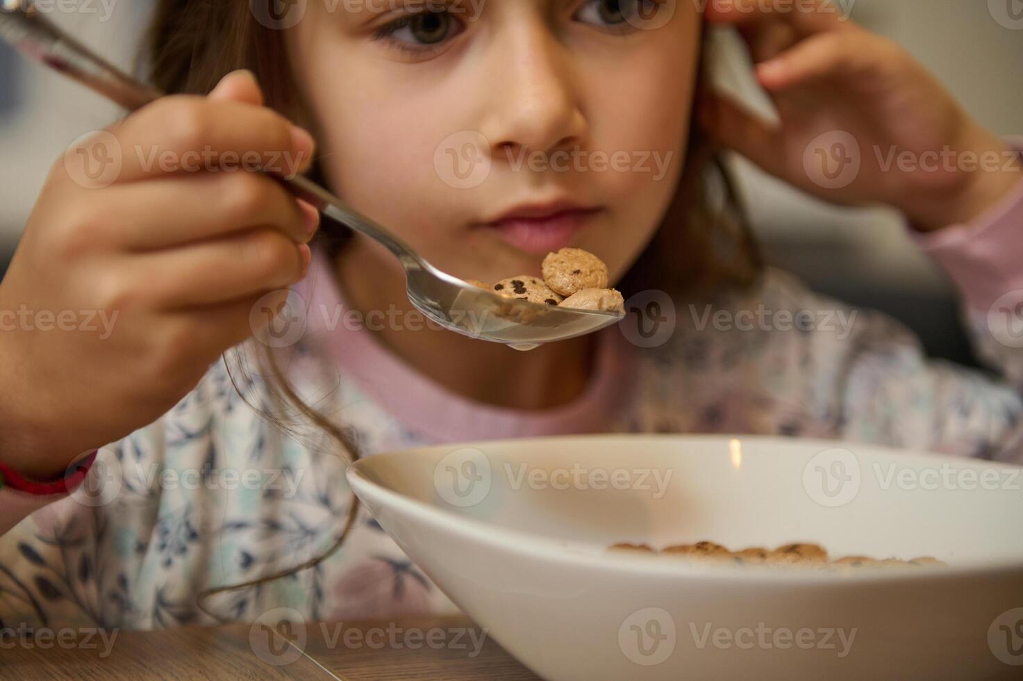 Close-up of a Caucasian little kid girl having her breakfast, eating oat flakes with milk. People and food concept photo