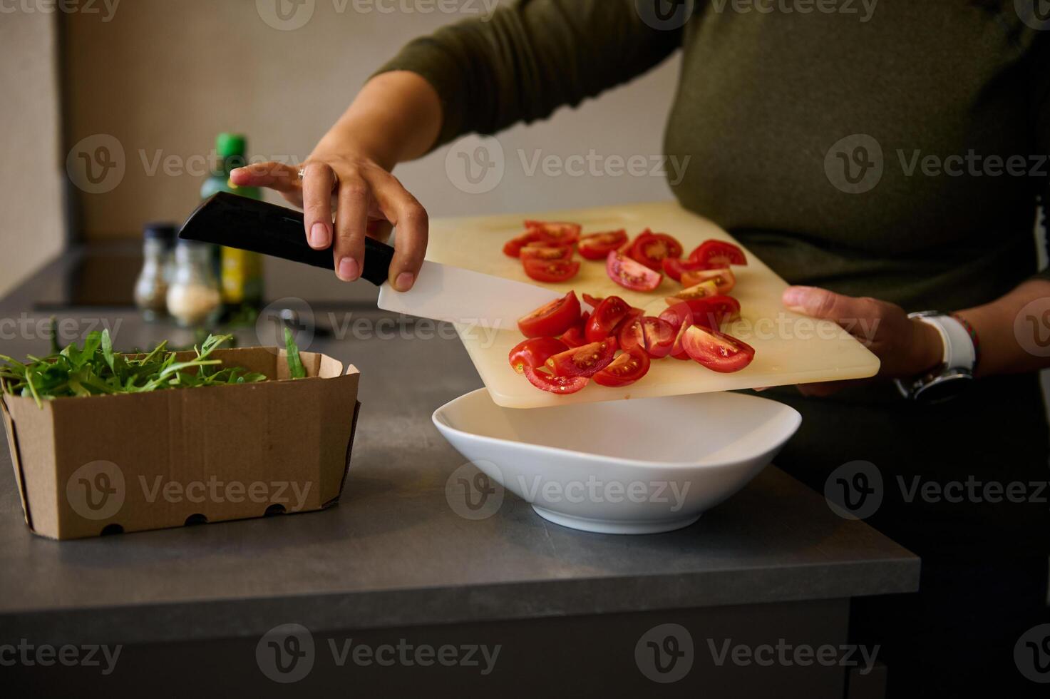 Chef hands with knife, cutting red tomatoes for salad. Fresh vegetables, arugula leaves and olive oil on the table photo