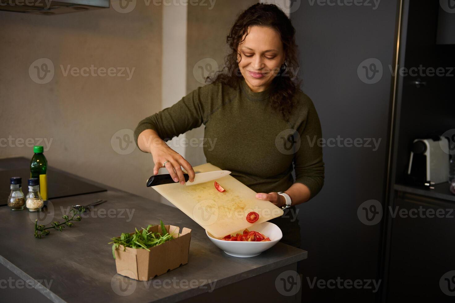 Housewife holding kitchen knife, chopping and pouring tomatoes into white bowl for salad, cooking healthy meal for lunch photo