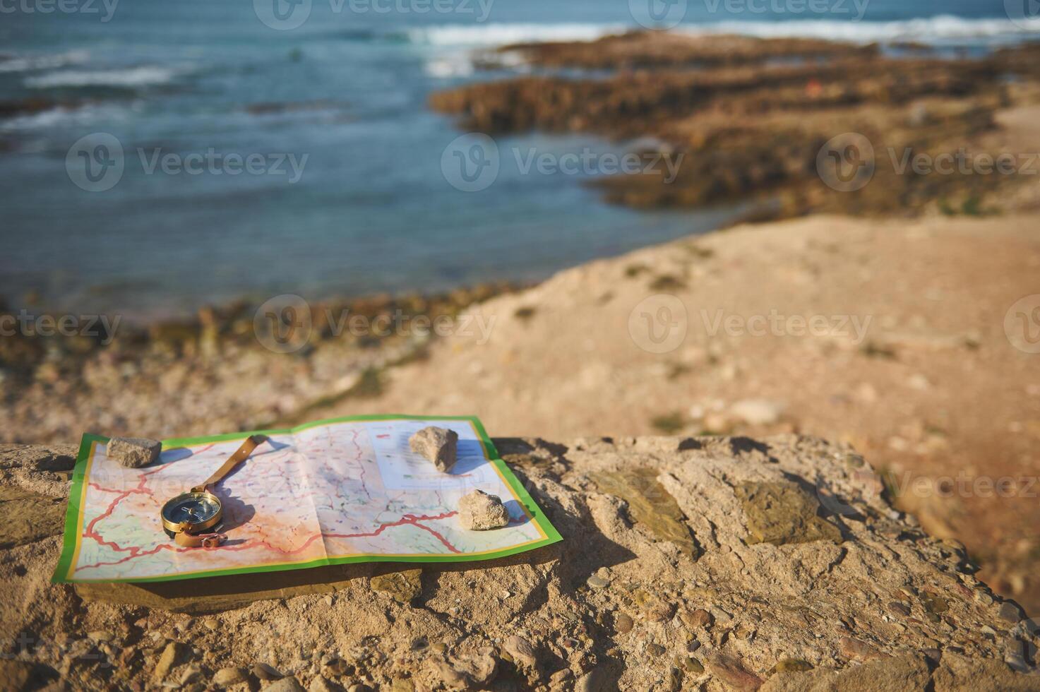 Still life with a golden compass on a geographic map lying down on the top of a rock overlooking seascape photo