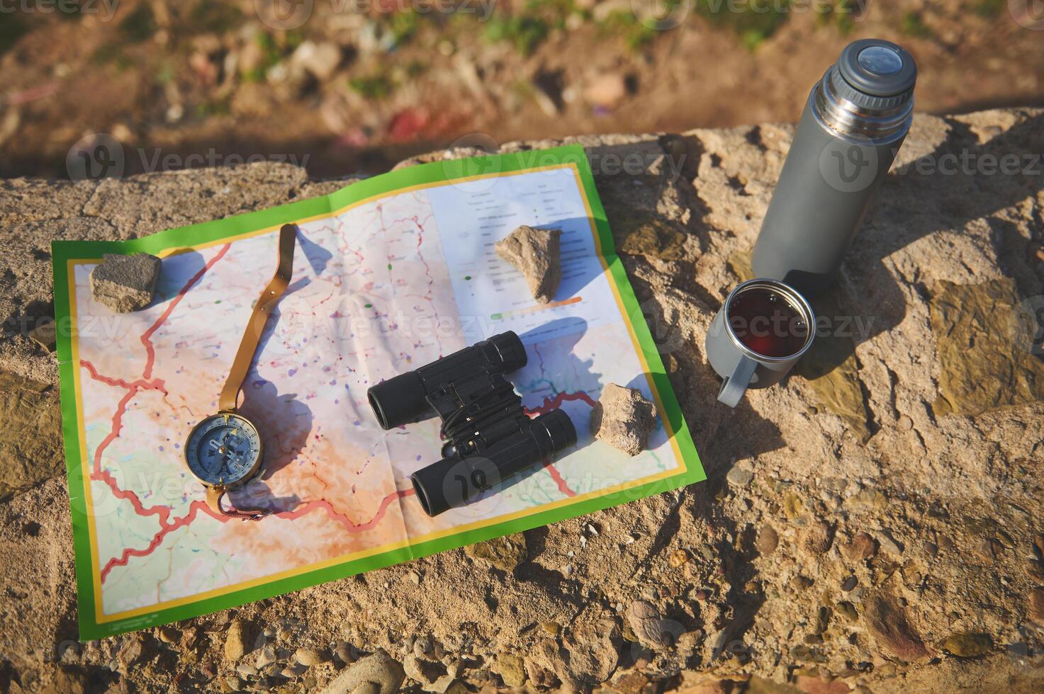 View from above of tourist's clothes, map, compass, binoculars and thermos flask lying down on the rock. Still life photo