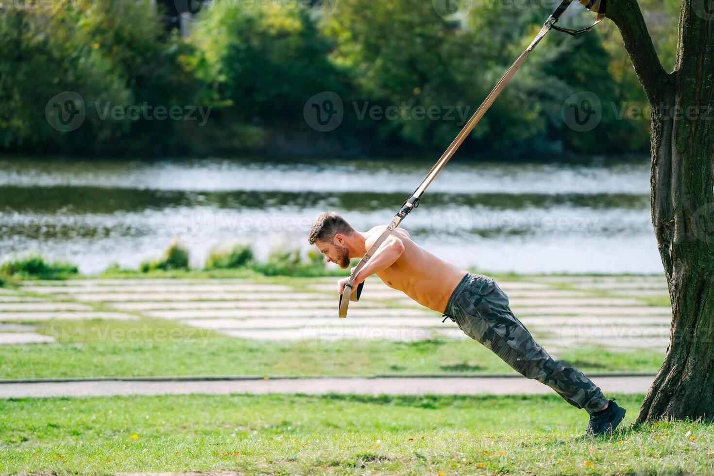 A Strong Man Embracing Nature's Strength. A shirtless man holding onto a pole in a park photo