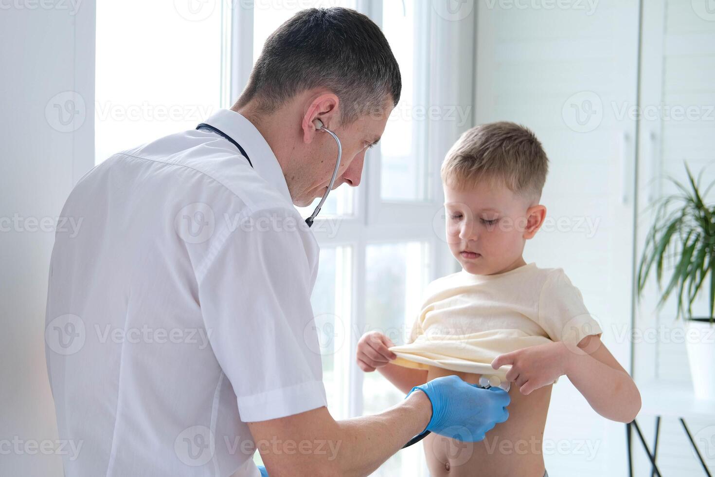 The doctor listens to the breathing of a little boy through a stethoscope. Pediatrician with stethoscope listens to the lungs of a child with bronchitis and cough photo