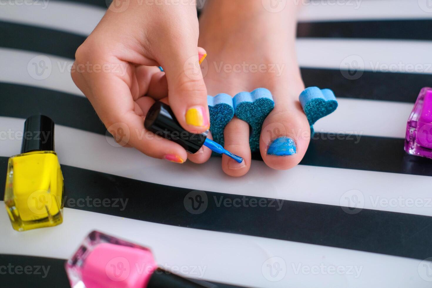 Children's feet with bright pedicure and manicure of different colors and bottles of bright nail polish. Little girl does a pedicure. Beauty salon game. Children's entertainment. photo