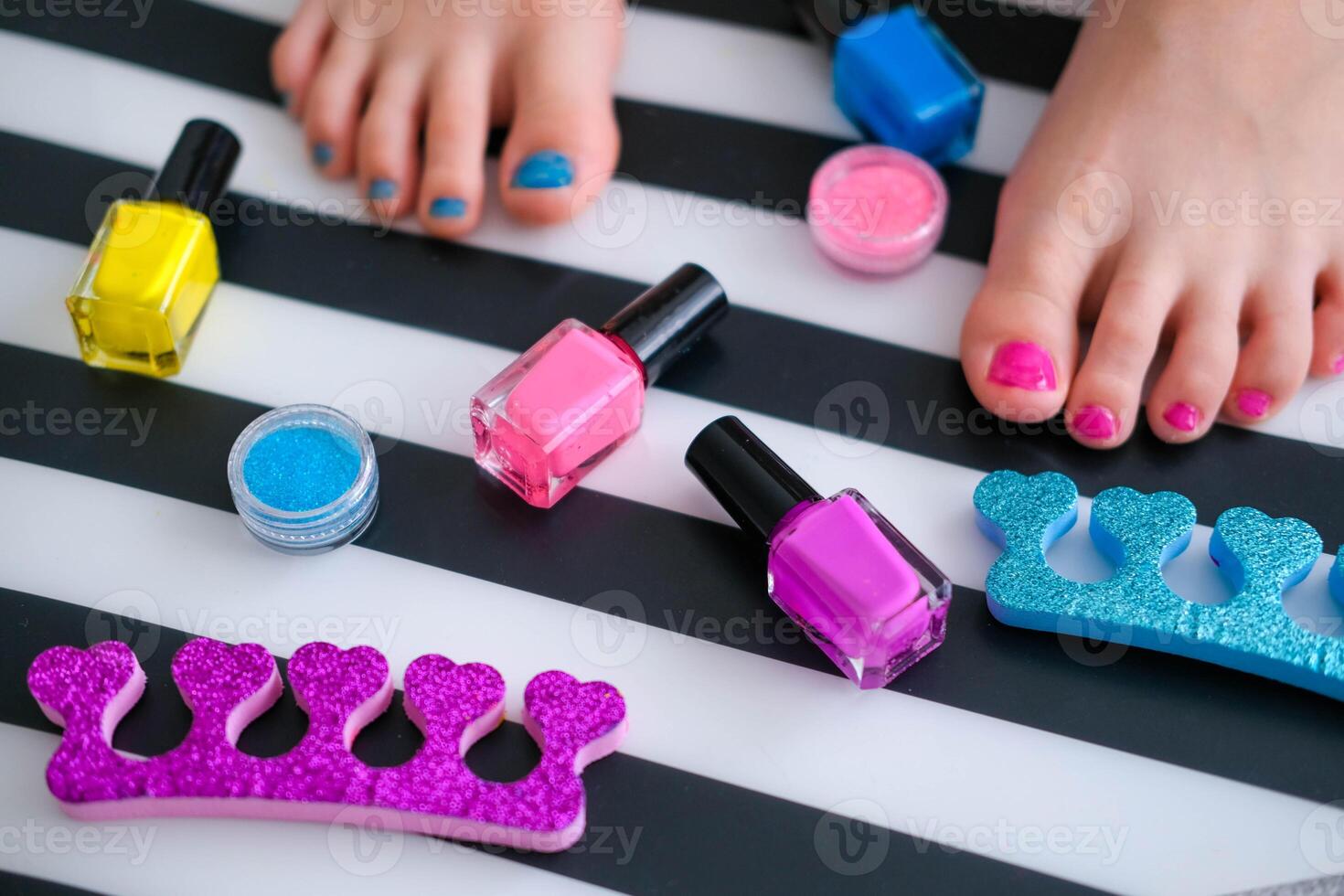 para niños pies con brillante pedicure y manicura de diferente colores y botellas de brillante uña polaco. pequeño niña lo hace un pedicure. belleza salón juego. para niños entretenimiento. foto