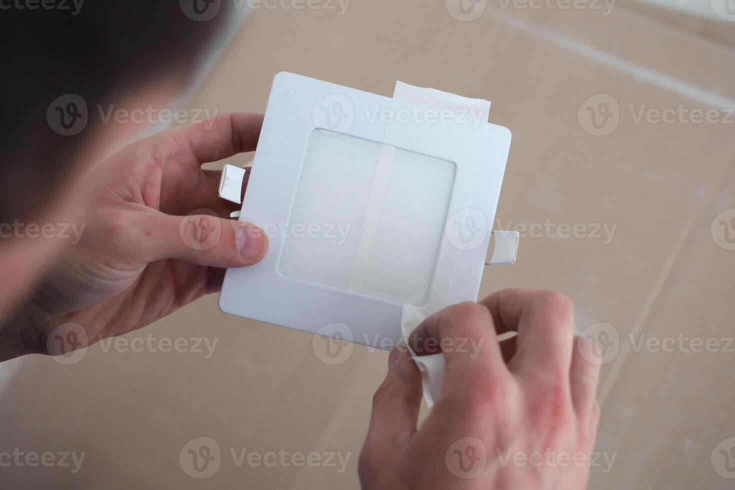 Step by step instructions for changing the color of the LED lamp. Men's hands remove masking tape from the lamp. Step 4 photo