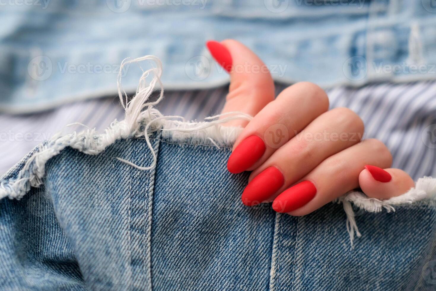 Beautiful female hands with a bright red matte manicure on a background of denim. Stylish oval nail design. Summer manicure. Copy space. photo