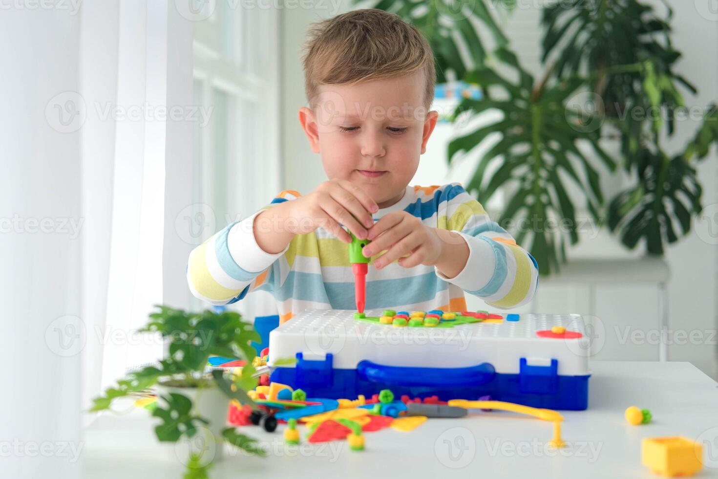 A little boy plays a set with a screwdriver and a drill, screws and parts. The child plays the builder spins the bolt with his hands, the development of imagination and motor skills. Educational logic photo