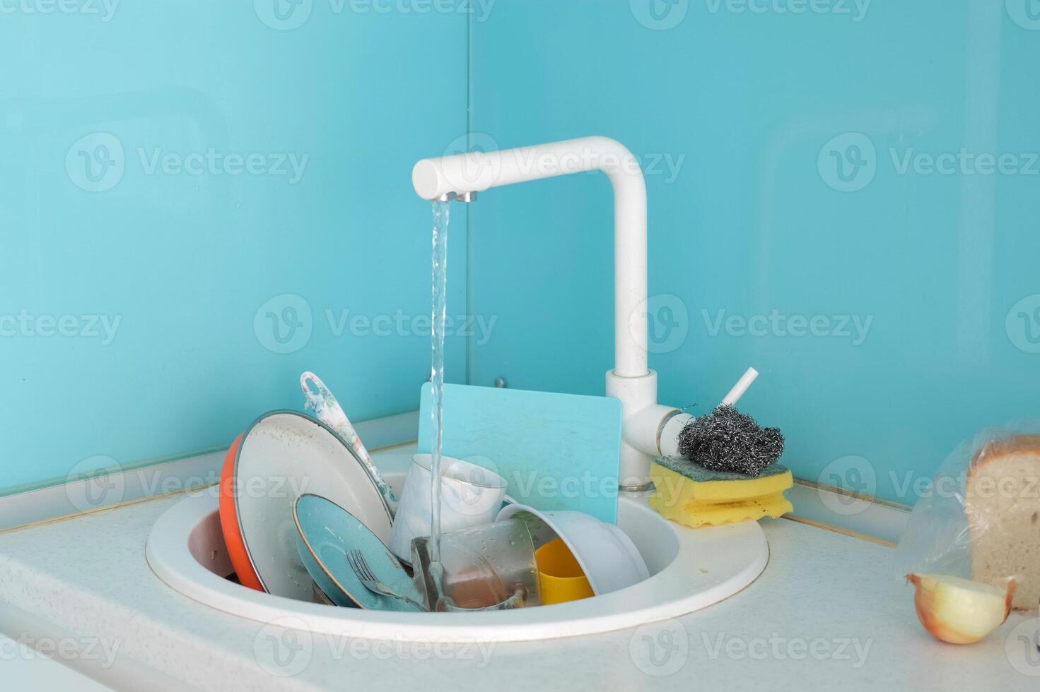 A sink full of dirty dishes in the kitchen. Water from an open tap flows into the sink. photo