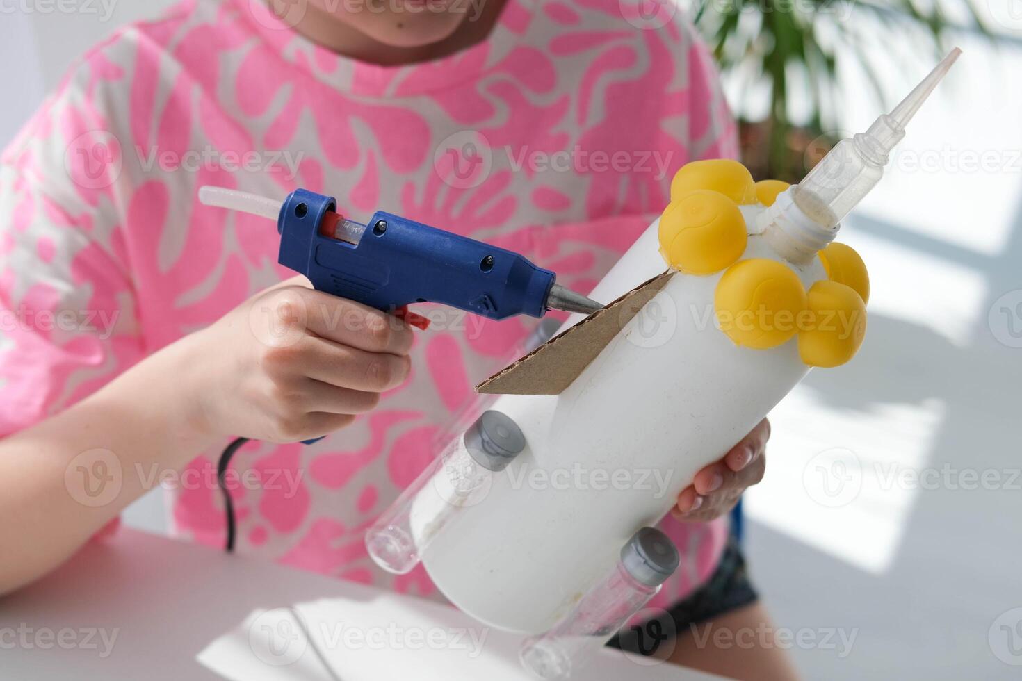 Step-by-step instructions for making crafts from improvised materials. Handmade at school craft rocket for the day of cosmonautics. The child is gluing parts to a plastic bottle. Step 15 photo