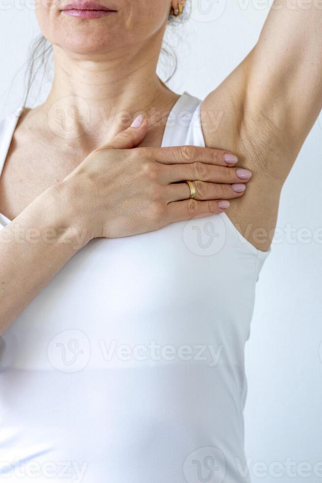 Shot of the woman in the white top against the white wall, performing self examination of the breasts, looking for abnormalities. Cancer awareness photo