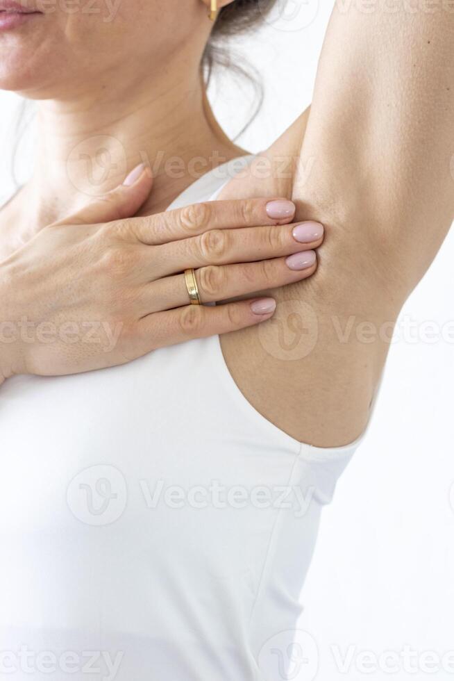 Shot of the woman in the white top against the white wall, performing self examination of the breasts, looking for abnormalities. Cancer awareness photo