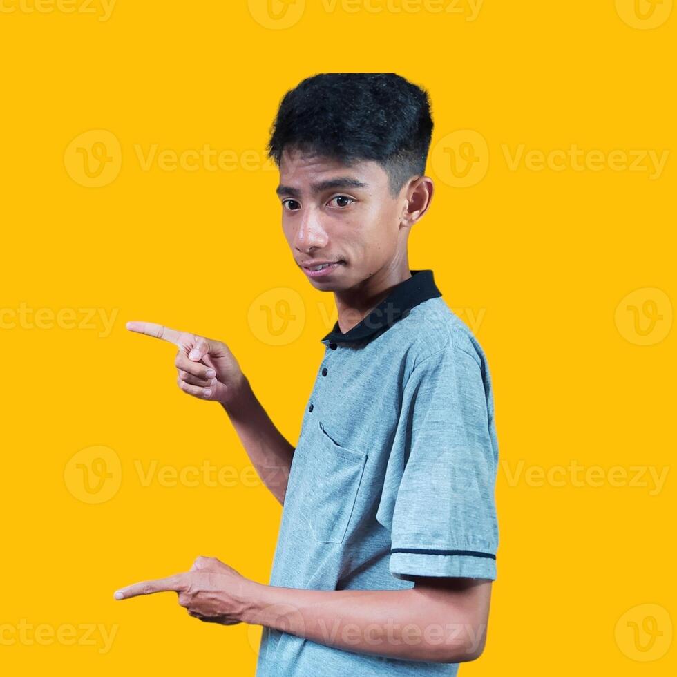 excited asian man wearing gray t-shirt pointing to the copy space on the side, isolated yellow background. photo