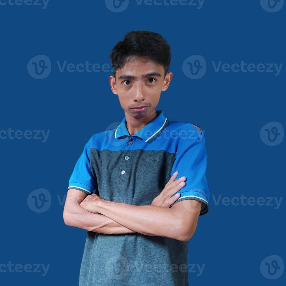 Asian man smiling confidently with folded hands. looking at camera isolated on blue background, wearing blue t-shirt photo