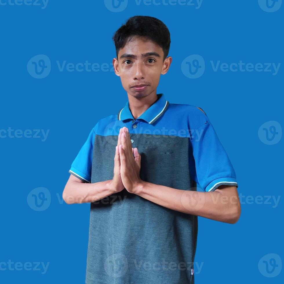 Young smiling asian man gesturing traditional gesture isolated on blue background. photo