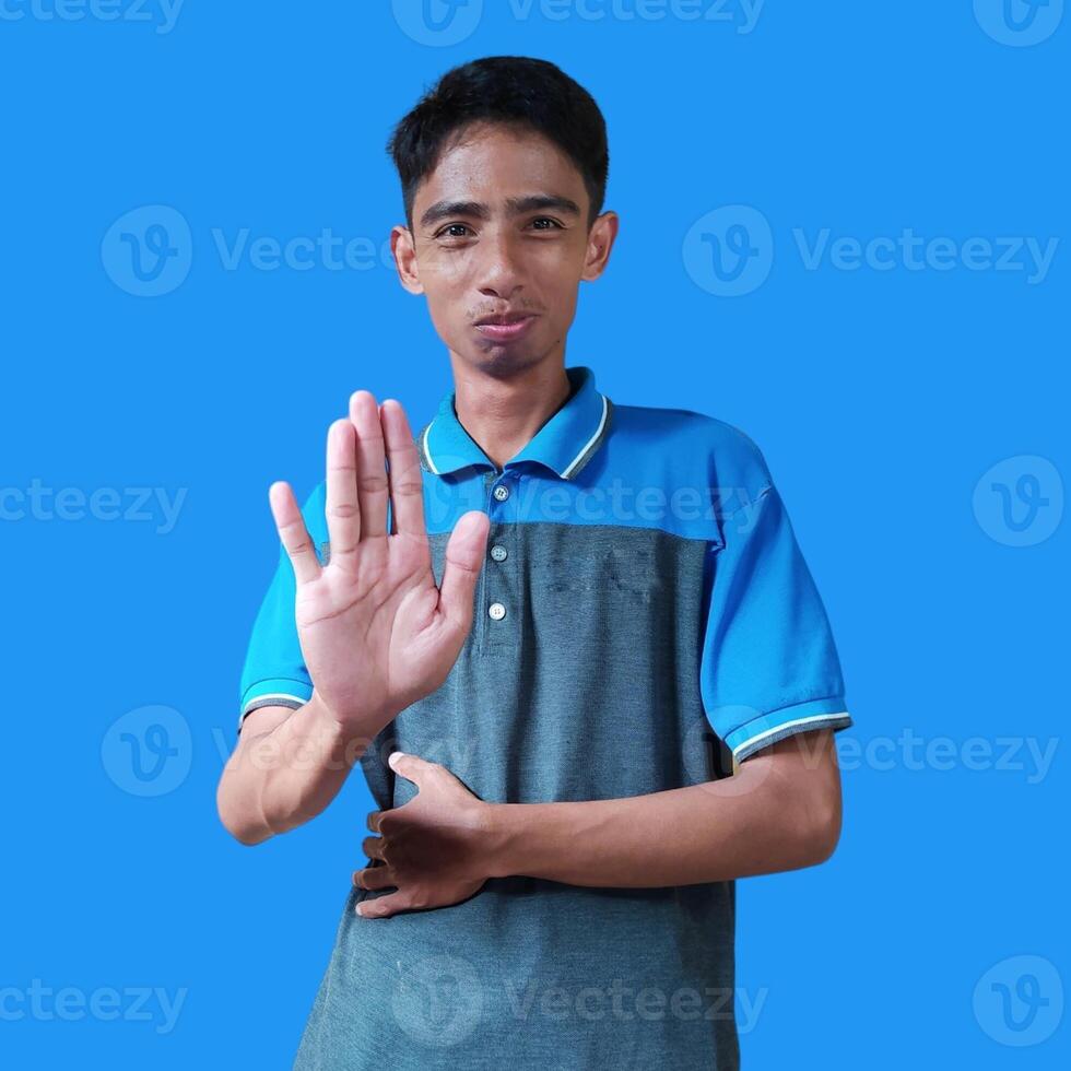 young Asian man with stop hand. with a serious face wearing a blue t-shirt, isolated on a blue background photo