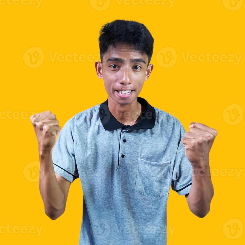 The enthusiastic face of the Asian youth clenched his fists. isolated on yellow background. photo
