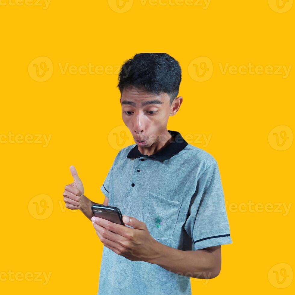 young asian man gesturing okay, one hand holding a smart phone isolated yellow background. photo