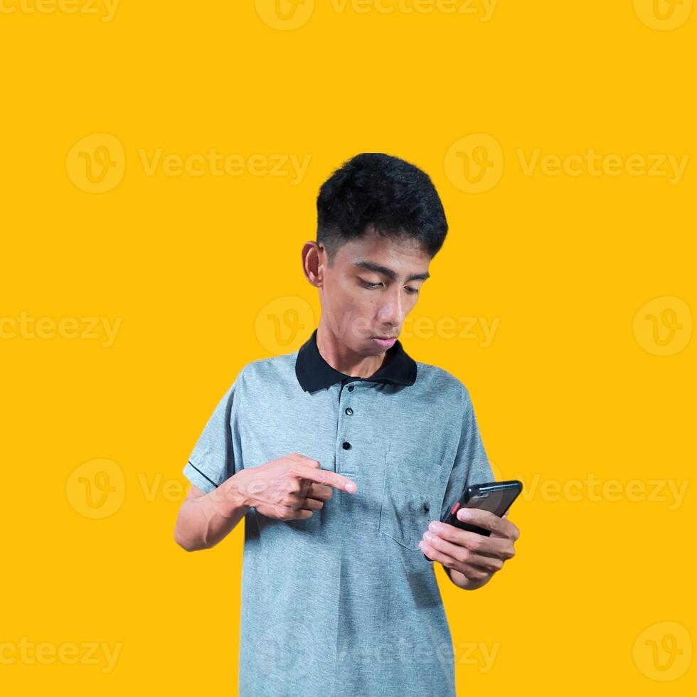 excited young man holding a smart phone wearing a gray t-shirt, yellow background. photo