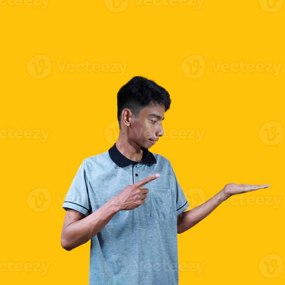 Excited Asian man wearing gray t-shirt pointing at copy space on the side, isolated on yellow background. photo