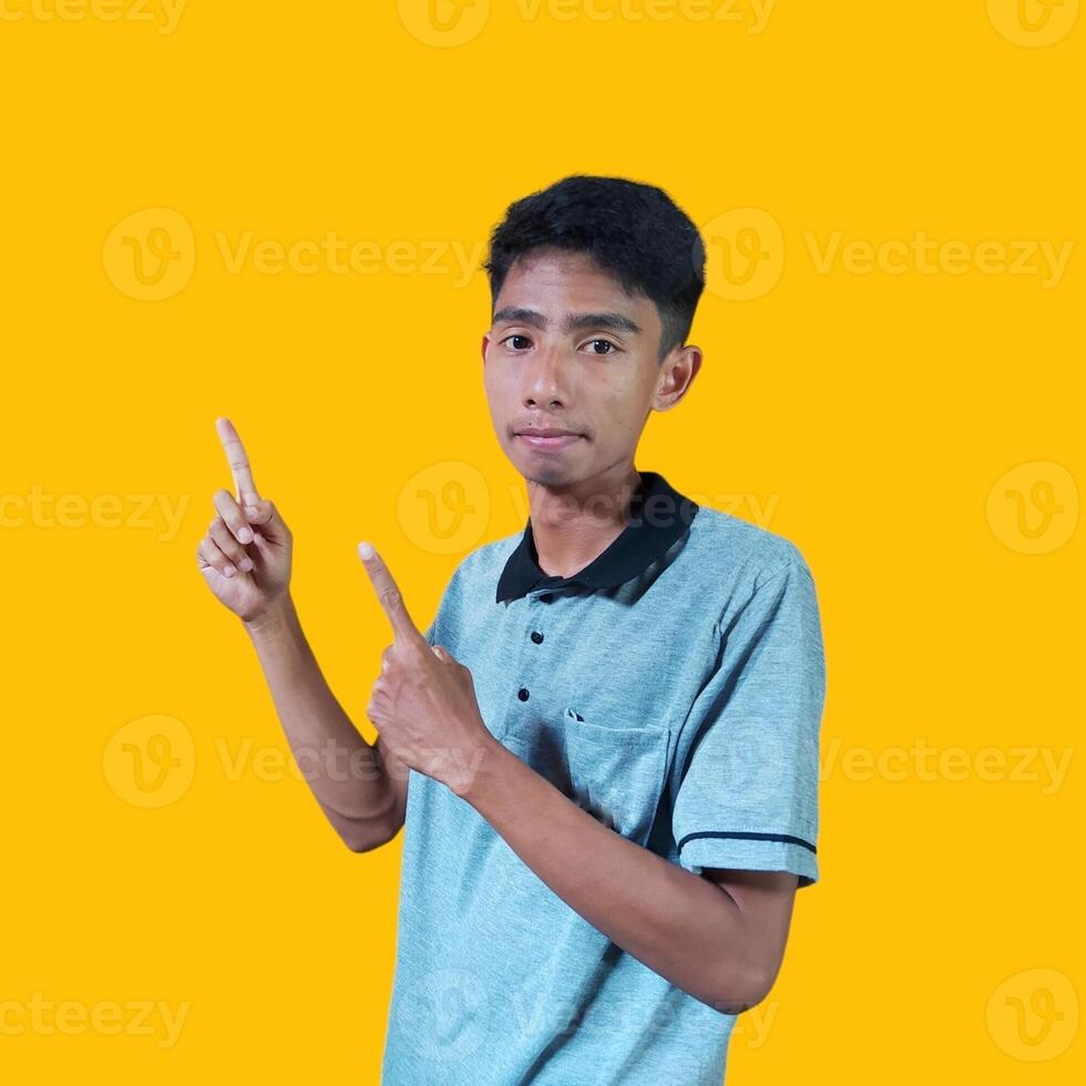 excited asian man wearing gray t-shirt pointing to the copy space on the side, isolated yellow background. photo