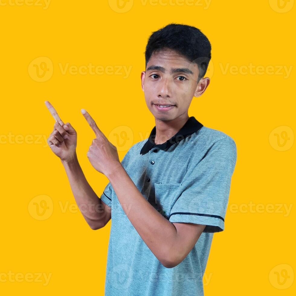 excited asian man wearing gray t-shirt pointing to the copy space on the side, isolated yellow background. photo