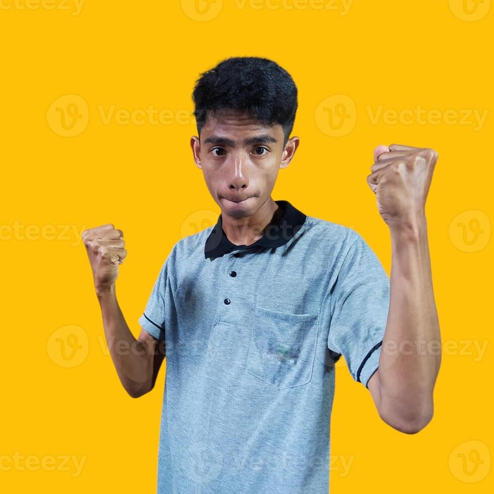 The enthusiastic face of the Asian youth clenched his fists. isolated on yellow background. photo