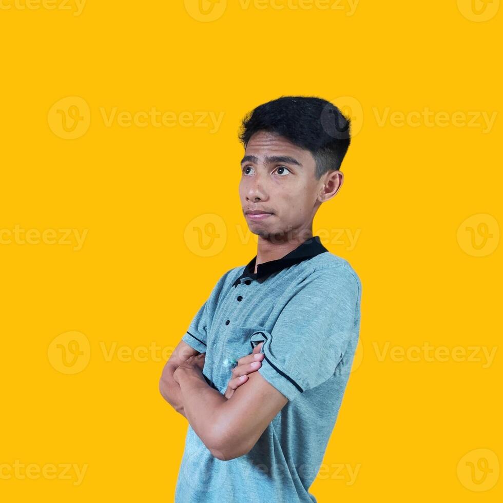 Thoughtful young Asian man hands folded thinking about something, wearing gray t-shirt on yellow background. photo