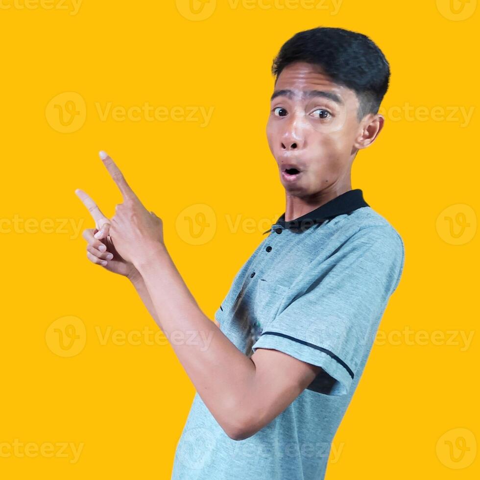excited asian man wearing gray t-shirt pointing to the copy space on the side, isolated yellow background. photo