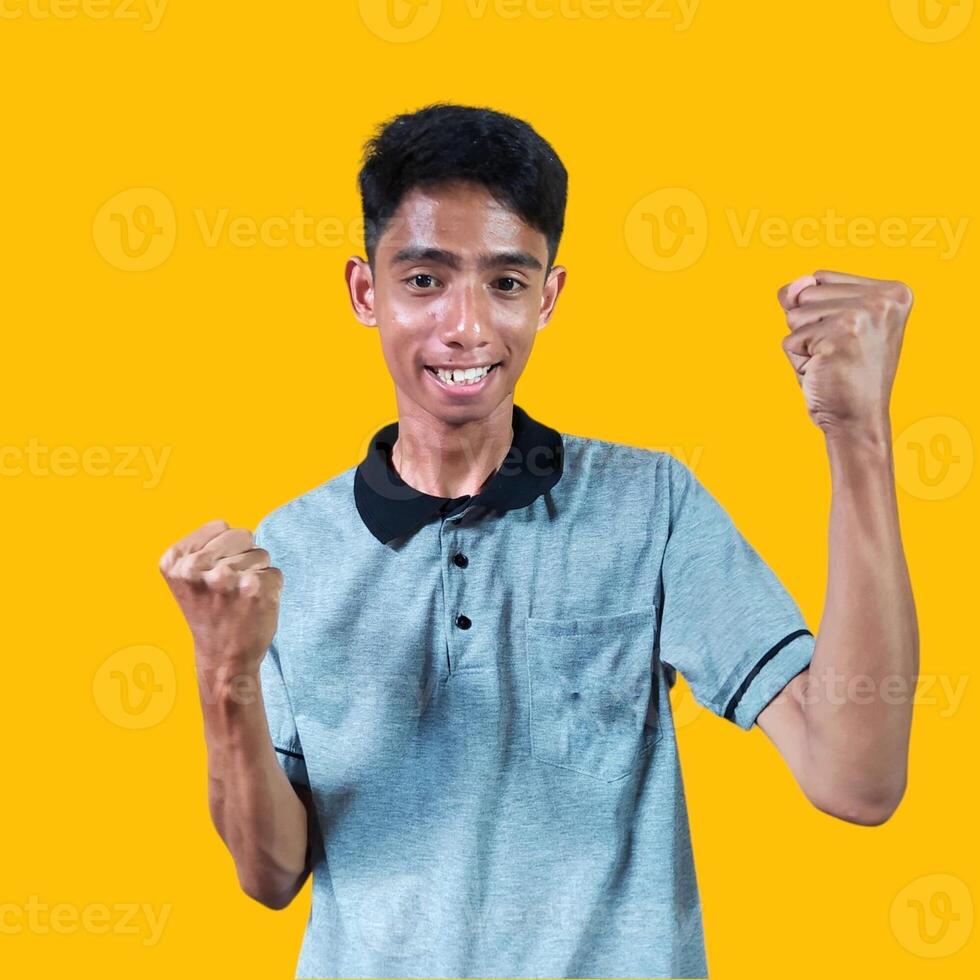 The enthusiastic face of the Asian youth clenched his fists. isolated on yellow background. photo