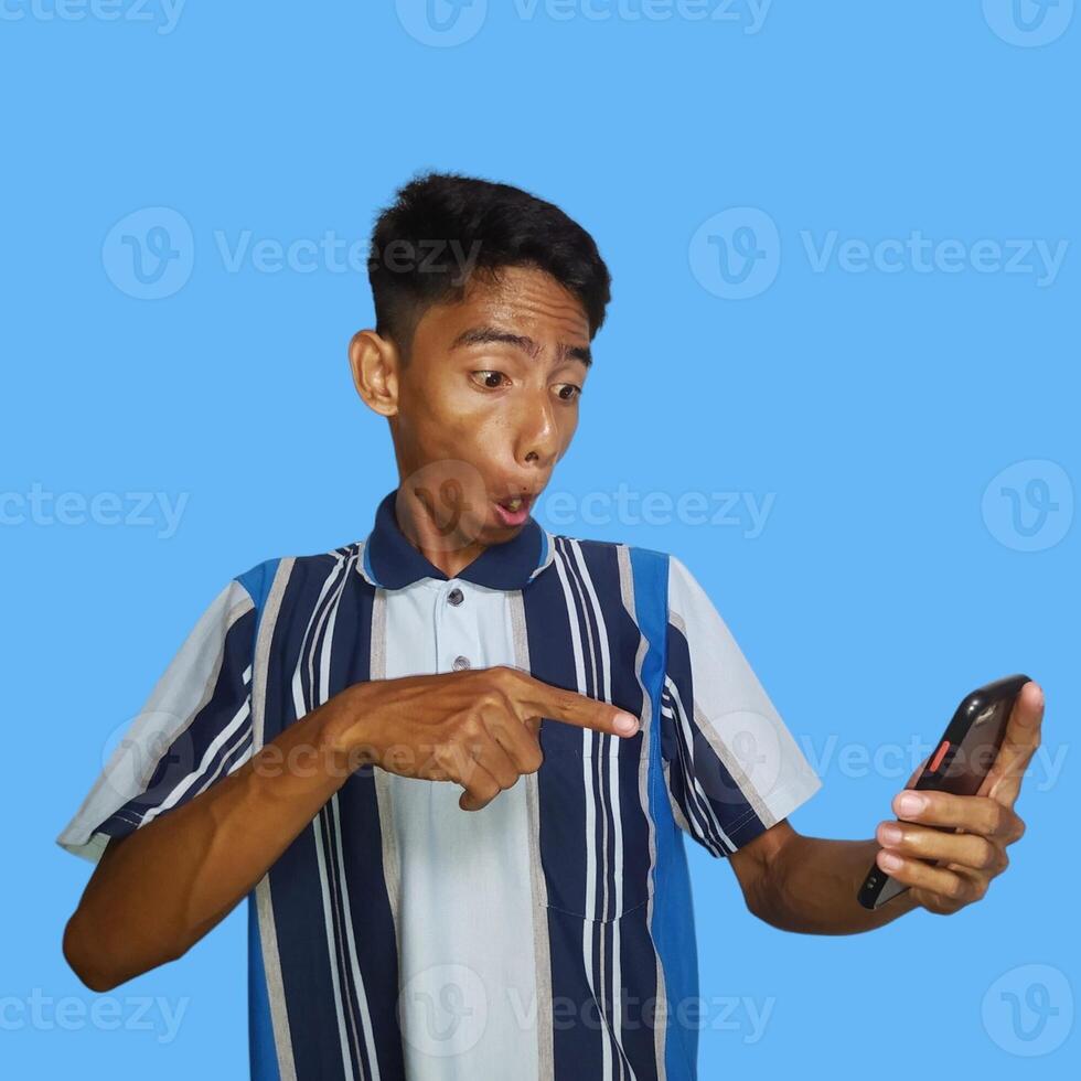 Young asian man surprised looking at smart phone in left hand holding isolated blue background photo