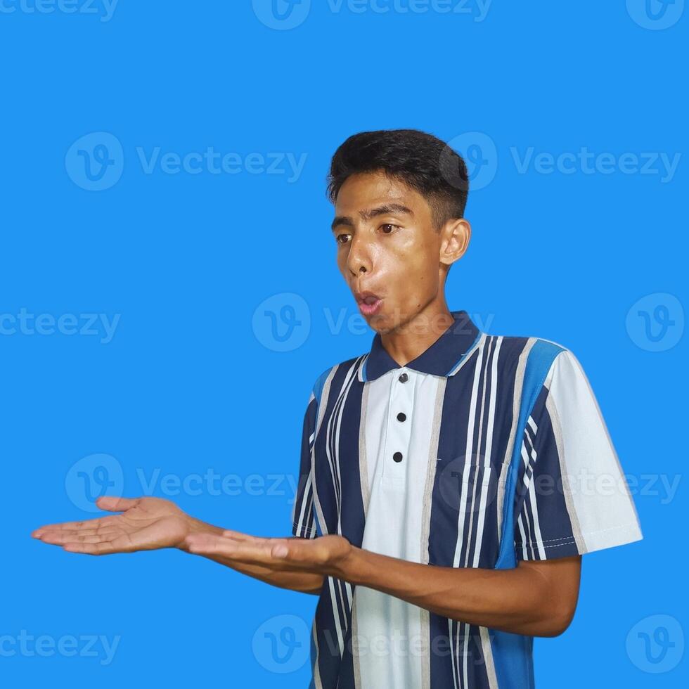 Excited Asian man wearing colorful t-shirt pointing at copy space on the side, isolated on blue background. photo