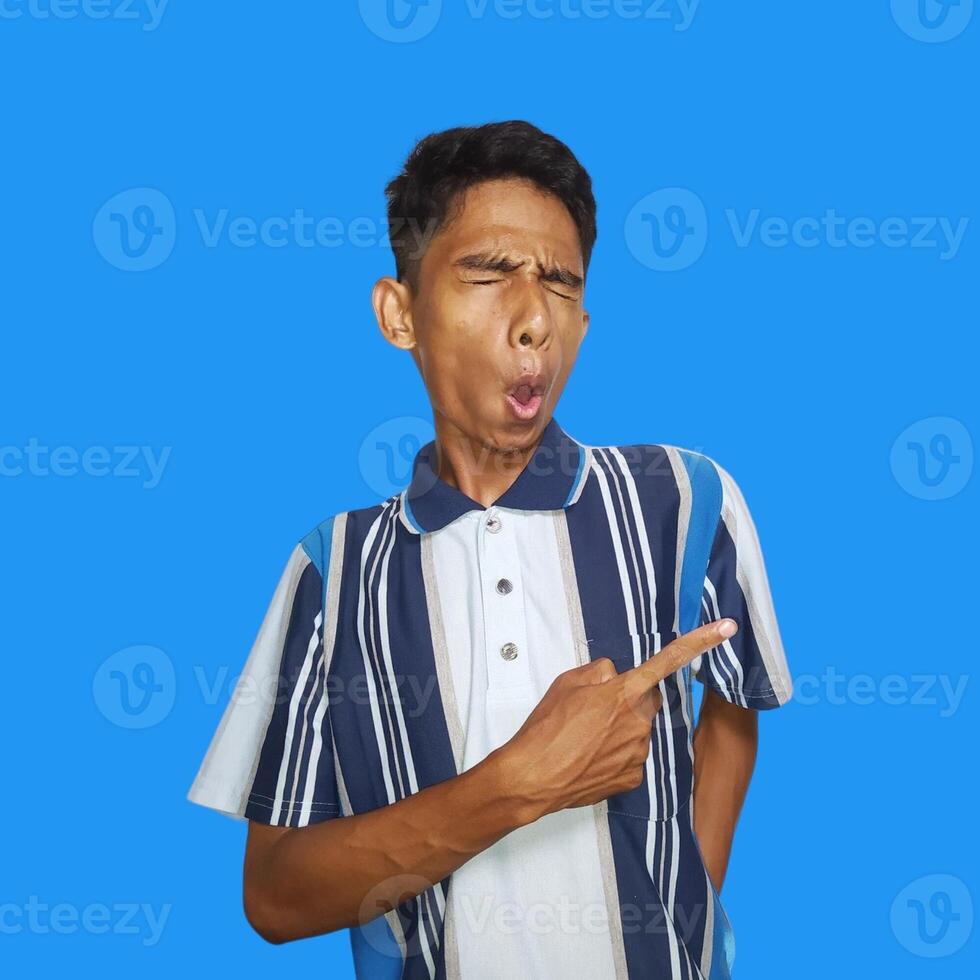 excited asian man wearing colorful t-shirt pointing to the copy space on the side, isolated blue background. photo