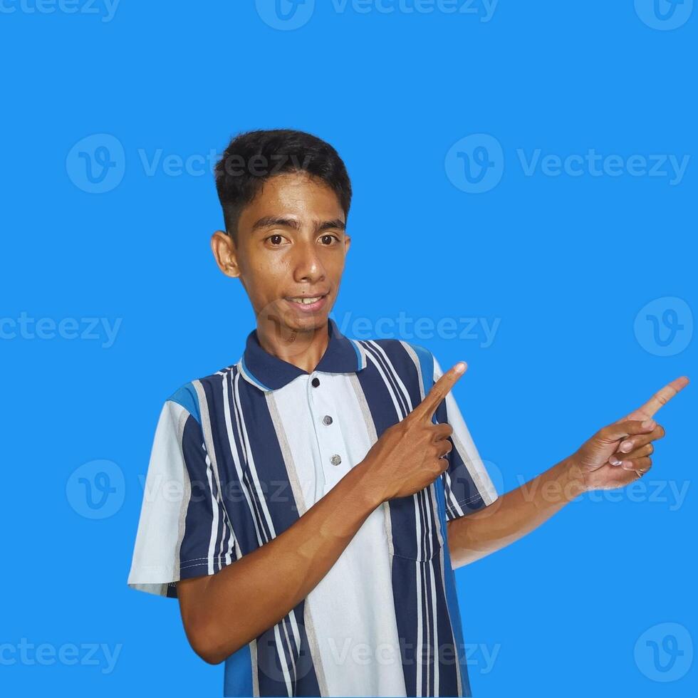 excited asian man wearing colorful t-shirt pointing to the copy space on the side, isolated blue background. photo