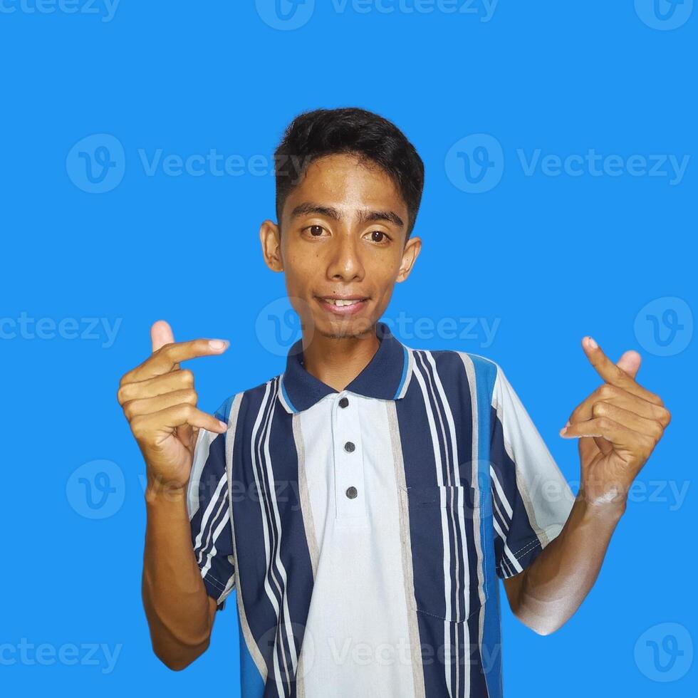 Young Asian man feeling happy and romantic forming heart gesture, wearing colorful t-shirt on blue background. photo